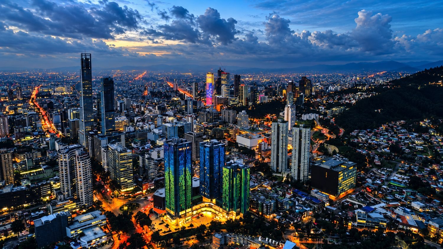 Panorámica aérea de Bogotá al atardecer, con las torres del centro financiero iluminadas y los cerros orientales al fondo
